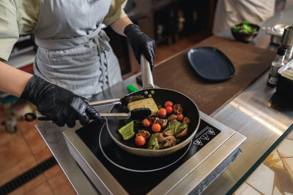 Chef cooking fried cheese with vegetables on frying pan in restaurant kitchen